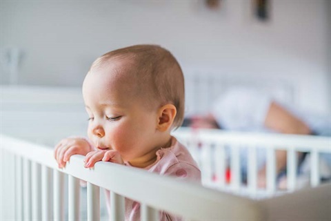 A toddler standing in a cot in the bedroom