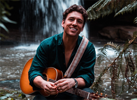 Taylor Henderson with his guitar in front of a waterfall