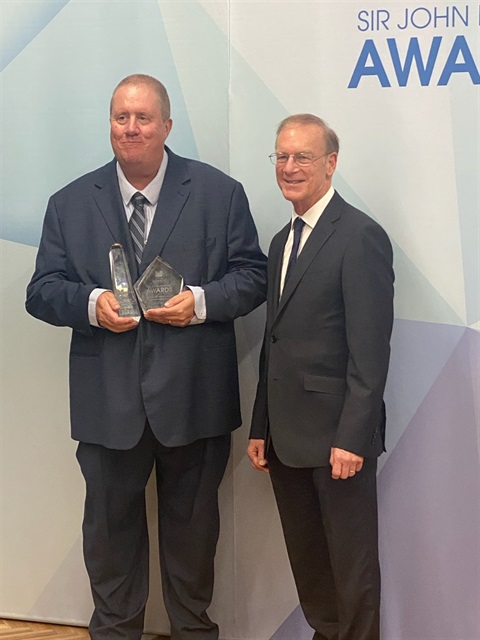 Outstanding Leadership award winner Philip-Ryan-in-a-blue-suit-and-tie-holding-two-glass-awards-and-Mayor-Brian-Little-in-a-suit-and-tie